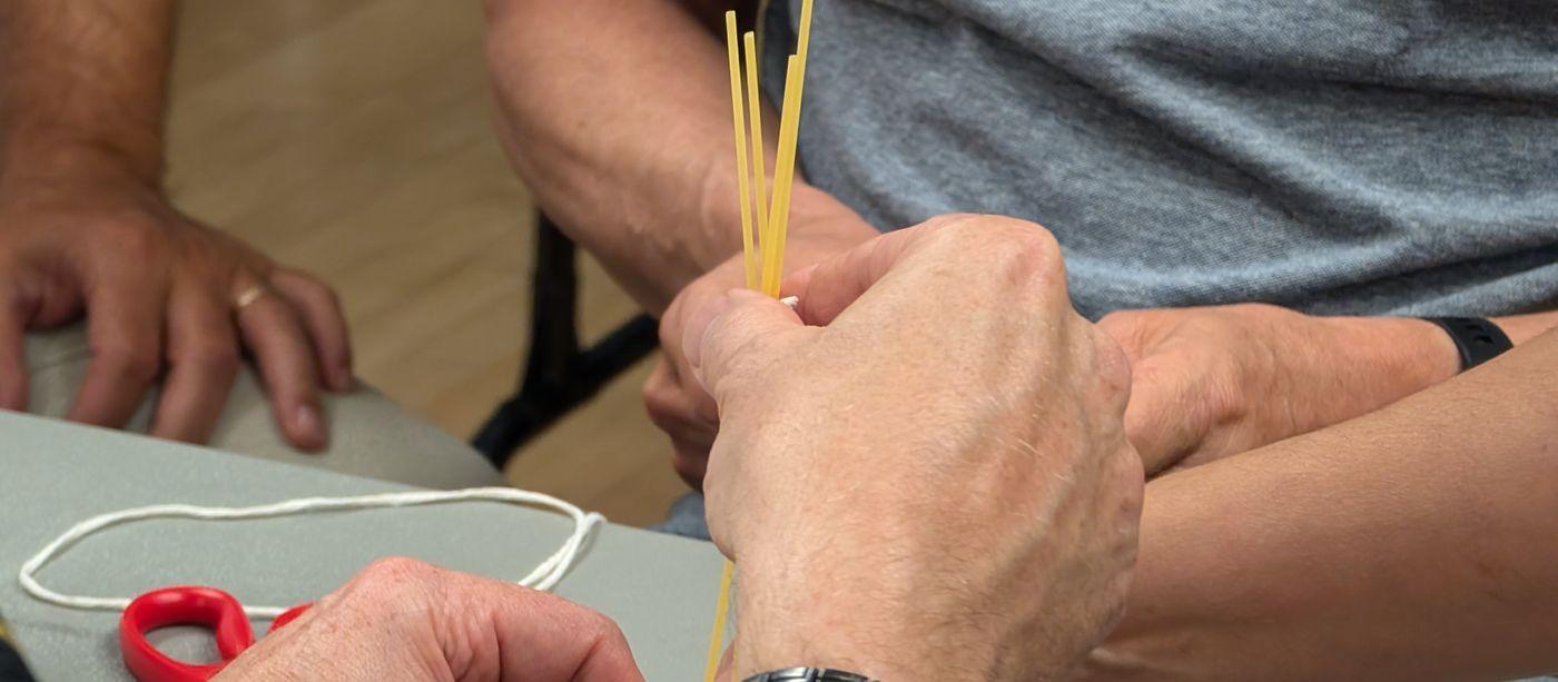 Hands building a structure from dry spaghetti and string during a team building exercise